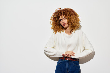 Portrait of a young woman with curly hair, expressing emotion in a casual outfit against a plain...