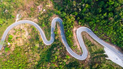 Aerial top down bending curve winding road path in the green forest 