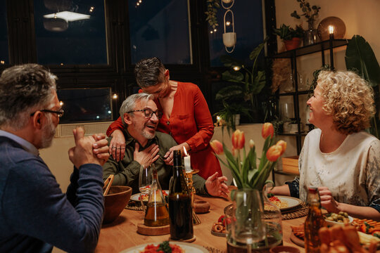 Woman Embracing Senior Man Celebrating with Friends at Dinner Table