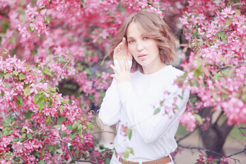 Fototapeta premium A woman in pink, in a cherry blossom garden in spring, a model posing, a soft spring photography
