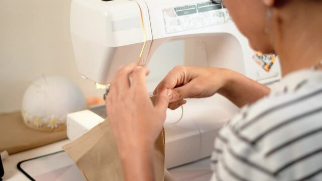 Close-up skilled hands guiding fabric through sewing machine, ensuring even stitches. Attention detail key in professional tailoring and handmade clothing production. Sewing tools, pins, seam ripper