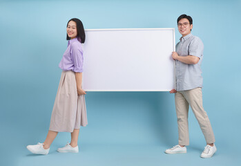 Group of young adults holding blank presentation board against a light blue background in a modern...