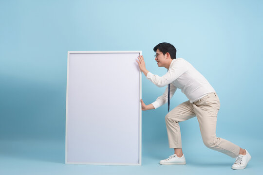 Young Asian man pushing a blank white board in a studio setting during bright daylight