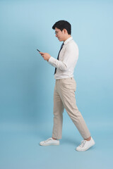 Young Asian man checking his phone while walking on a blue background during daylight