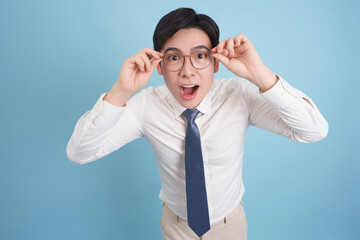 Young Asian man surprised while adjusting glasses against a light blue background in a casual studio setting