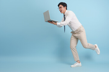Young man running in a formal outfit while holding a laptop and laughing against a light blue background