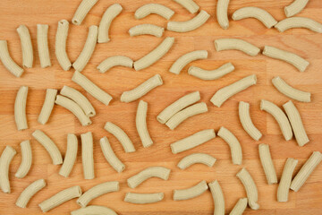 A top-down view of scattered homemade spinach pasta tubes on a wooden surface