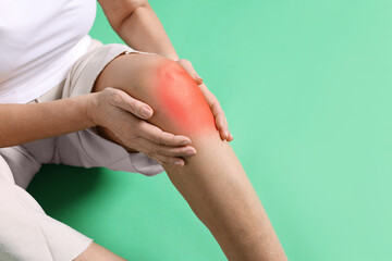 Senior woman suffering from pain in knee on green background, closeup
