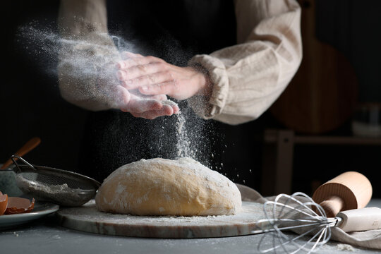 Woman dusting flour over dough at grey table, closeup - Powered by Adobe