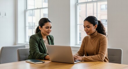 Two female office friends laughing at workplace, having fun, talking at laptop, discussing funny creative ideas, brainstorming, chatting, enjoying business friendship