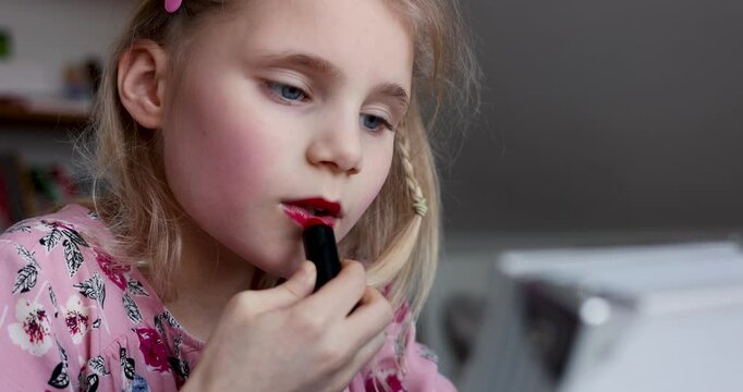 little girl applying red lipstick. child doing makeup yourself at home