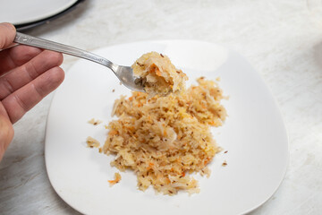 Hand holding a fork with pickled cabbage on a white plate soft focus close up