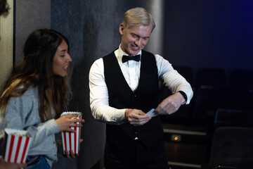 Smiling usher checking tickets of people with popcorn entering movie theater