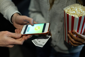 Usher scanning digital ticket on smartphone with popcorn bucket in background