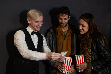 Usher checking tickets of couple entering movie theater with popcorn