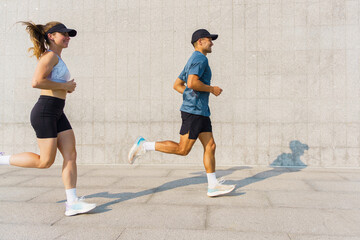 Fototapeta premium Couple jogging side by side along a concrete pathway in a sunny urban environment