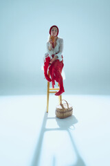 Young woman sitting on wooden stool, holding bread near face, gazing into distance, symbolizing...