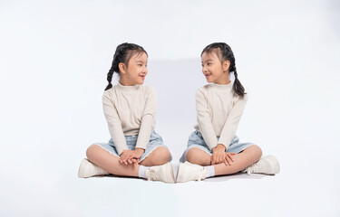 Two young girls sitting in a cross-legged position looking at each other and smiling on a clean white background.