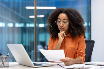 Serious thinking woman financier doing paperwork inside office. Focused accountant holding documents and papers in hands. Businesswoman checking data, working inside office