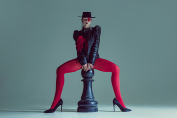 Fierce figure in structured black clothing and dramatic red details straddles oversized chess...
