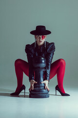 Woman gripping chess piece, wide stance, intense gaze, exuding dominance and control. Concept of...
