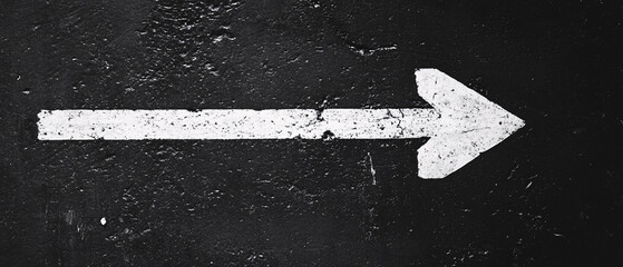 A white right-facing arrow painted on a worn black asphalt surface indicating direction movement and navigation in an urban environment
