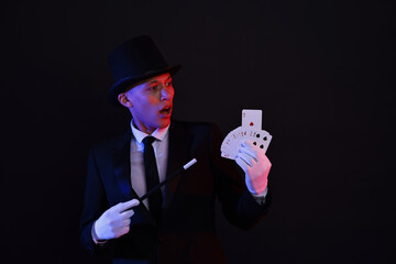 Illusionist pointing magic wand on playing cards against black background, space for text