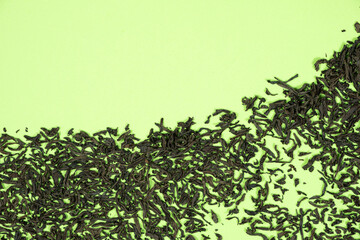 Top view of dried black tea leaves on green background, place for text