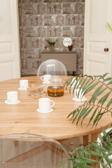 A peaceful arrangement featuring a glass teapot, cups, and a vase of white tulips on a wooden table, evoking warmth, simplicity, and serenity in the decor.