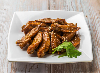 Honey Glazed Chicken Wing Tips with savory sauce, sesame seeds and cilantro served in plate on Wood Table Close up Side view of Hong Kong food