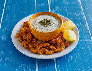 crispy fried clam strips with a lemon and caper tartar sauce on a white plate