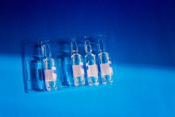 Ampoules with injectable solutions lie on a blue background, illuminated by sunlight. A symbol of medical precision, pharmaceuticals, and sterility.