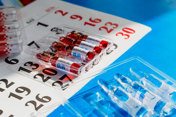 Ampoules with injectable solutions lie on a blue surface with a calendar in the background. A...