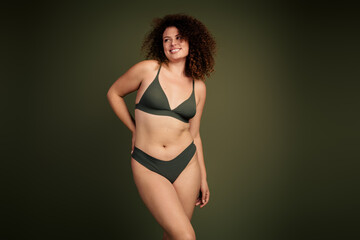 Obraz premium Confident young woman in green bikini on khaki background emphasizing natural curves and positive body