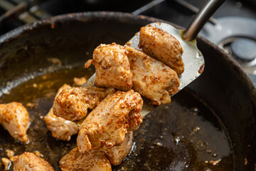 Chicken fillet pieces are fried in a frying pan in sauce and spices and turned over