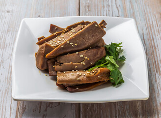 Spicy Sliced Pig Tongue with rich sauce, sesame seeds and cilantro served in plate on Wood Table Close up Side view of Hong Kong food