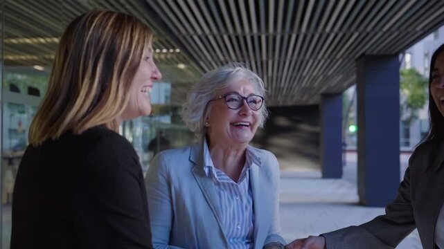 Cheerful group of mature businesswomen gathering outside work office laughing together. Empowered female having fun.