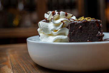 Chocolate brownie slice with whipped cream and chocolate sauce on a white plate