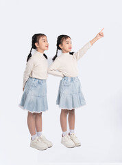 Naklejka premium Two young girls dressed alike, one pointing upwards, with similar outfits, on a clean, white background.