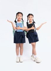 Naklejka premium Two young schoolgirls in uniform with books and backpacks present towards the camera on a white background