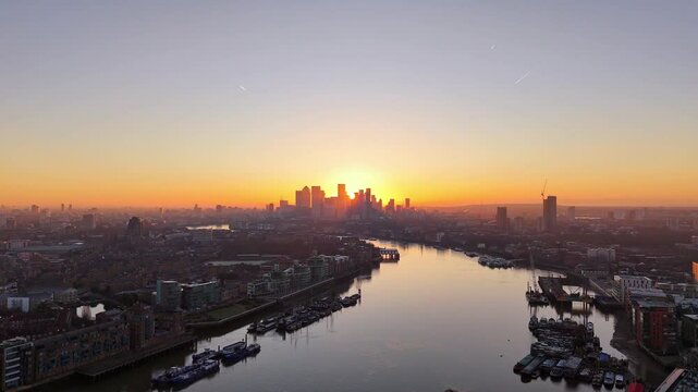 Sun rising over the skyscrapers in Canary Wharf, London, UK, the river Thames in the foreground