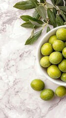   White bowl with green olives next to green olive cluster on marble counter