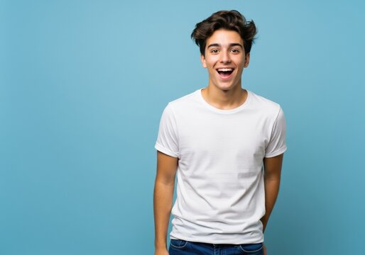 Happy young man in a white t-shirt against a blue background expressing joy and positivity.