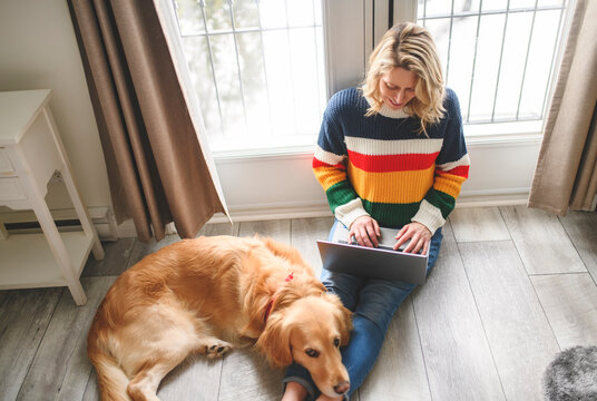 Portrait of woman using laptop computer with healthy golden retriever dog indoors in at home.