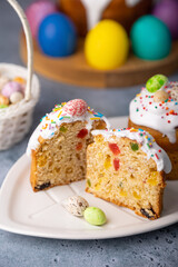 Two small Easter kulichs with candied fruits in white glaze with colorful sprinkles in the cut. Painted chicken and quail eggs. Traditional Easter baking. Easter holiday. Close-up, selective focus.