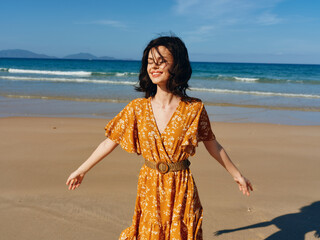 Woman in orange dress standing on beach with arms outstretched in sunny weather enjoying freedom...