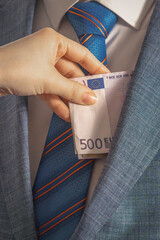 Hand drops European currency banknotes into the pocket of a man in a suit and tie standing in front of him. To give a bribe. Corruption