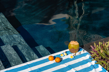 erfrischender Pool mit blau-weiß gestreiften Badetuch zwei Mandarinen eine geschälte Kokosnuss...