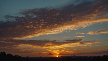 Obraz premium Spectacular sunset with orange and yellow clouds filling the sky over dark silhouette of trees and distant mountains, tranquil landscape