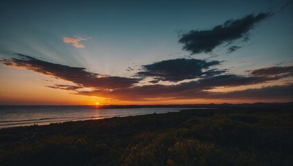 Fototapeta premium Striking Sunset Over Ocean Coastline with Dramatic Clouds and Sun Rays Illuminating the Sky and Landscape